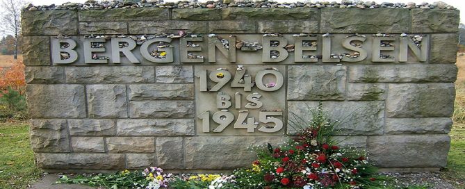 A photograph of a large stone memorial engraved with "Bergen-Belsen 1940-1945". Flowers and wreaths have been placed on the ground