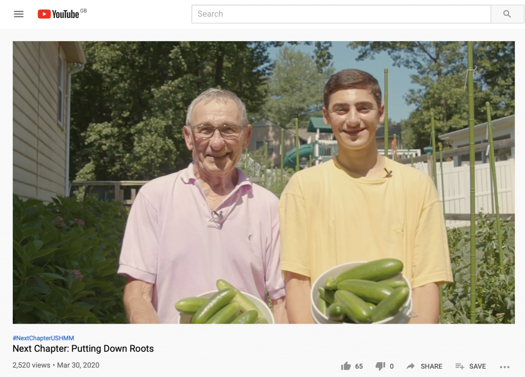 Nat and his young grandson stand shoulder to shoulder holding pots of cucumbers with a proud expression on their faces 