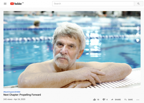 A Holocaust Survivor with grey hair holds onto the side of the pool and looks directly into the lens of the camera