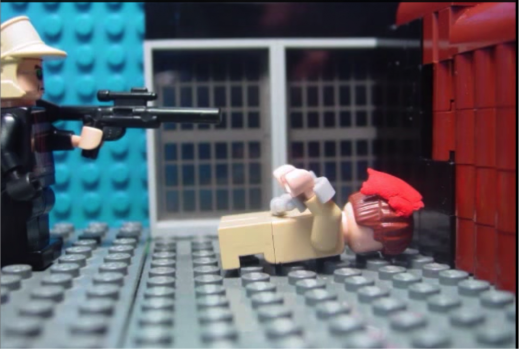 A lego scene of a man in black uniform shooting another, who is on the ground. The latter has red plasticine on his head symbolising blood.