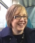 A woman with short light brown hair and glasses smiles on a train.