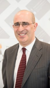 A bald man with glasses, wearing a suit smiles.