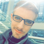 A young man with slick short hair, glasses and a nose piercing smirks at the camera.