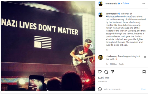 A guitarist plays in front of a large sign that says 'Nazi Lives Don't Matter' with an upside down US flag in monochrome.