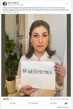 Woman with makeup and tiny brown hair wearing a white blouse holds a sign up that says hashtag we remember.