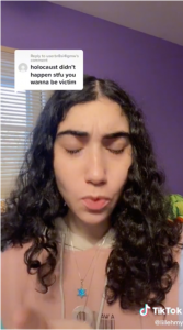 A young women with curly long black hair looks downwards. A reply post contains text top left: holocaust didn't happen stfu you wanna be victim.