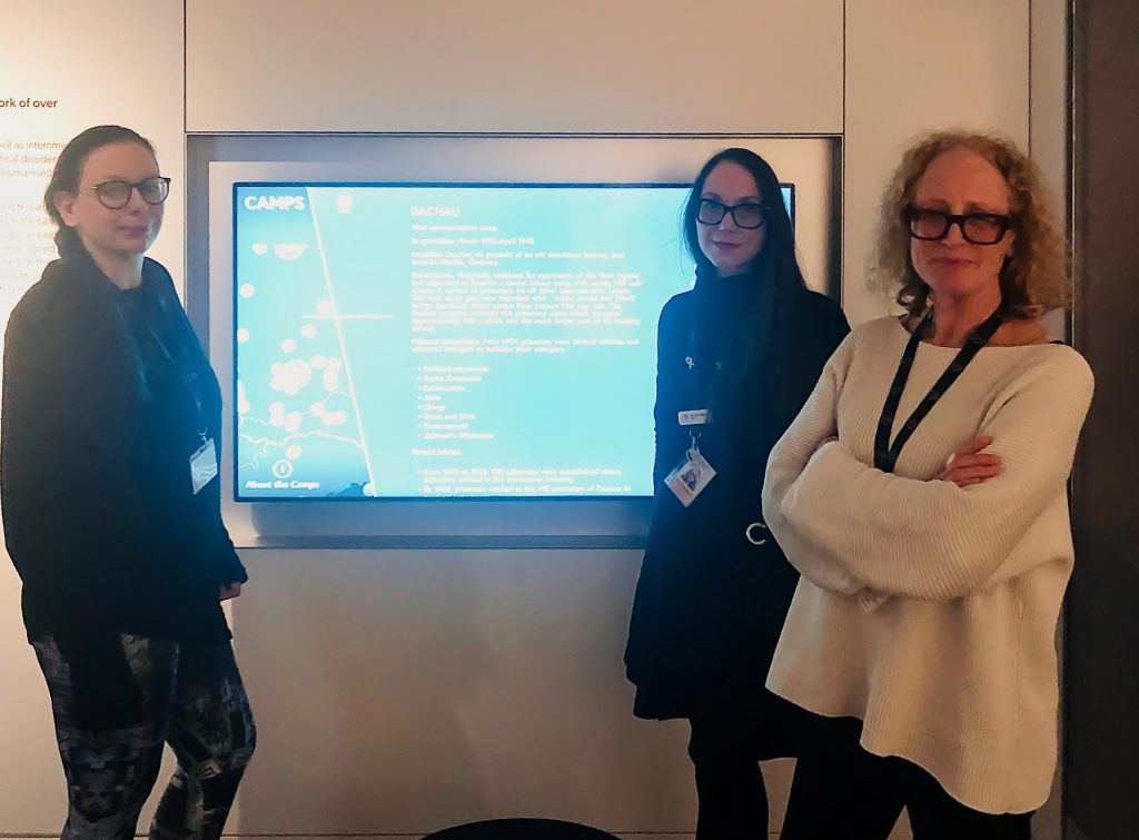 Three women stand next to a digital screen in a museum.