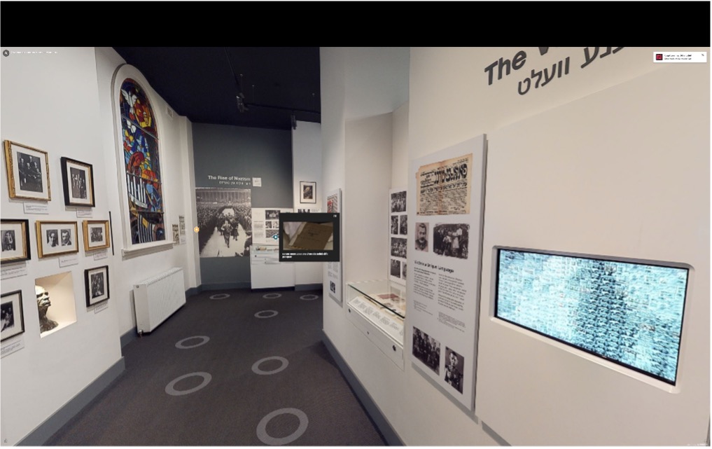 A museum corridor with framed photographs, information panels and a video screen. 