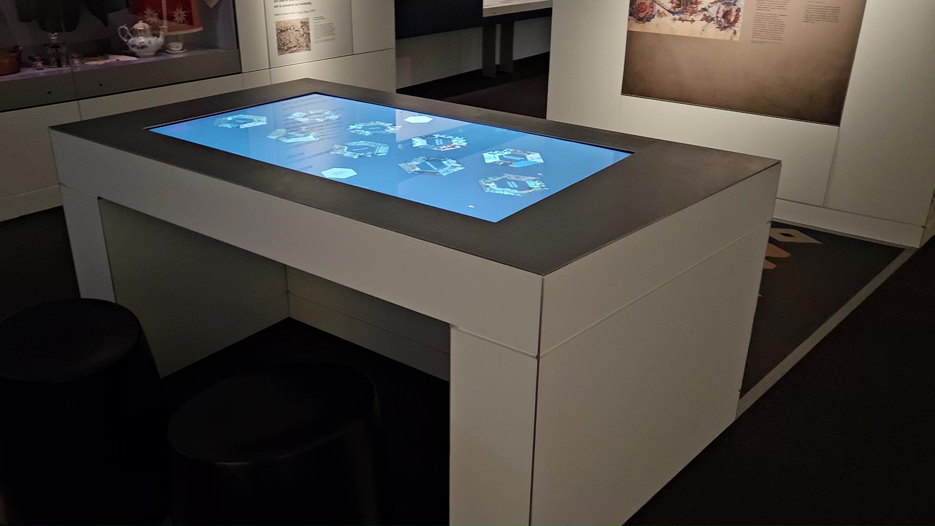 A table with a blue interactive screen in a museum exhibition space. Display content unreadable.