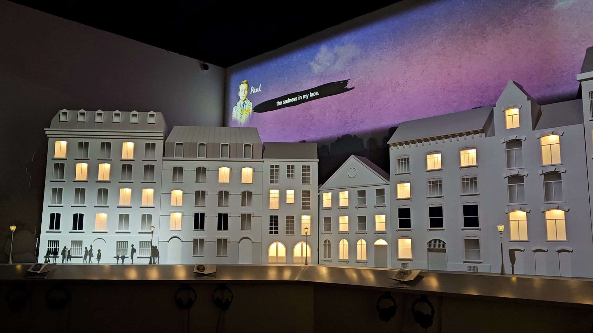 A white diorama montaging the architecture of different European cities. There are lights on in windows, and a digital display in the skyline. 