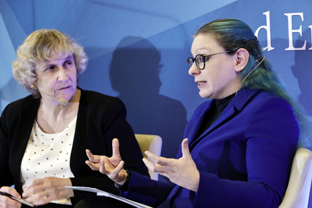 A blue hair woman speaks in front of a woman with white hair. 