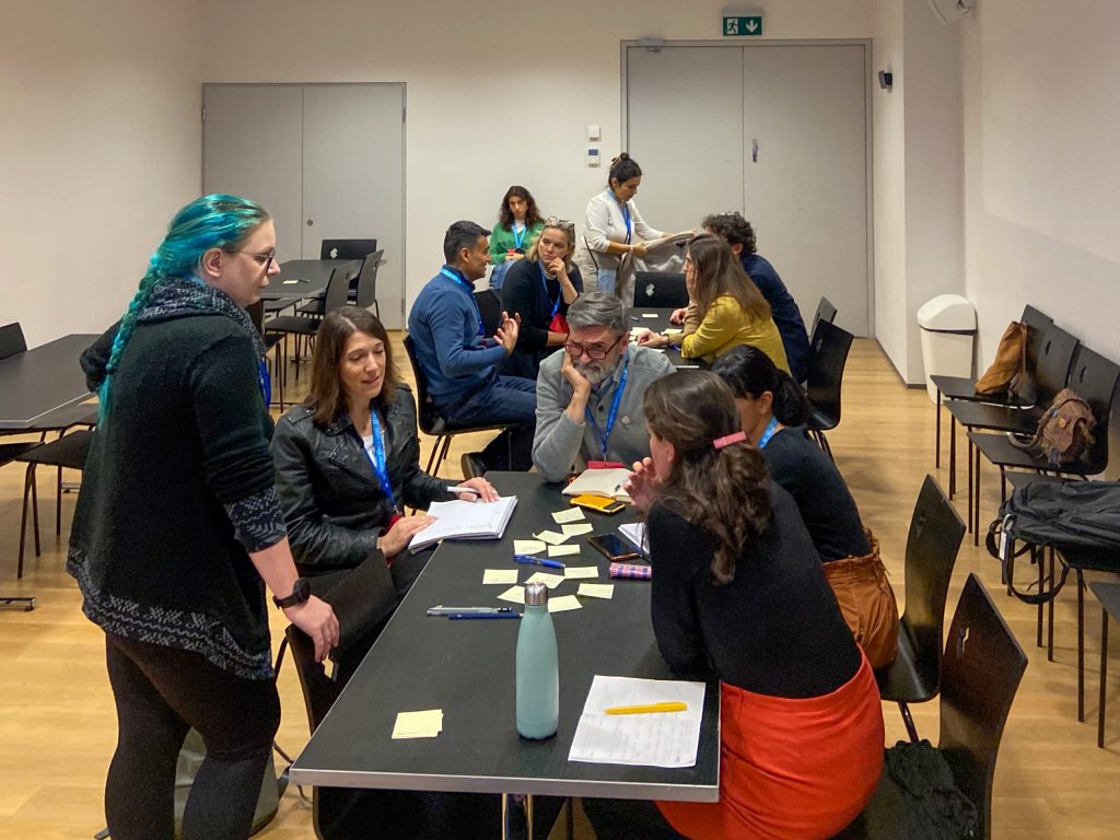 Two groups of museum professionals discuss post-it notes on their tables.