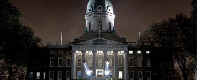 An imperial building with a canon in the foreground, lit at night.