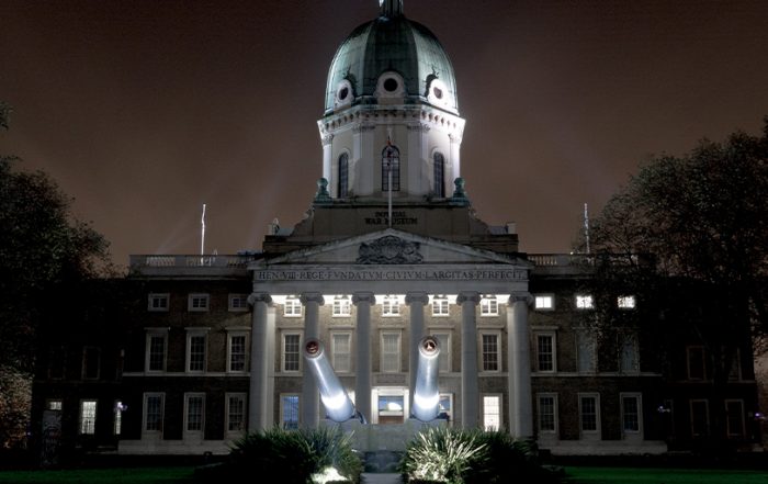 An imperial building with a canon in the foreground, lit at night.