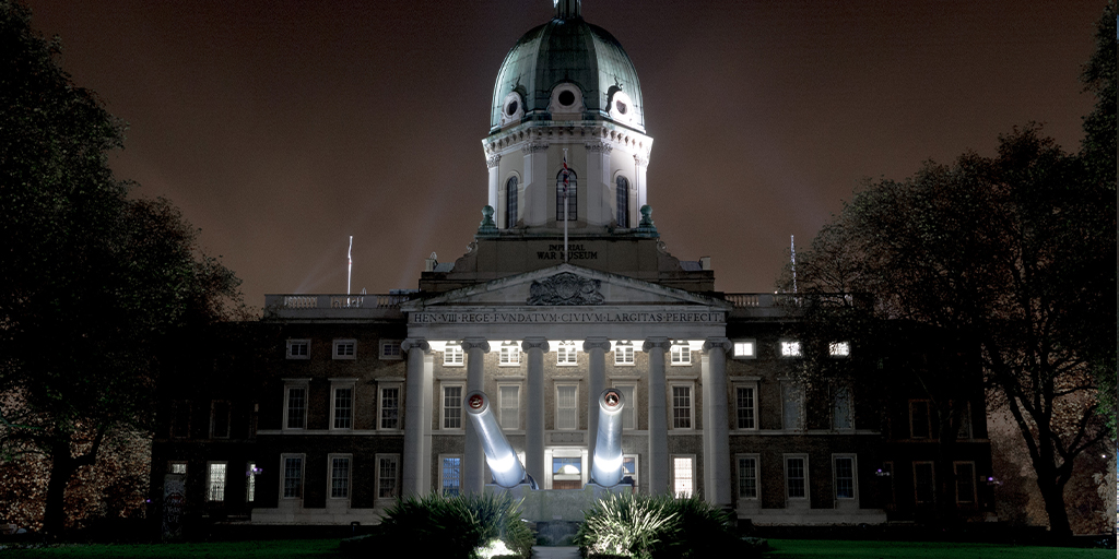 An imperial building with a canon in the foreground, lit at night.