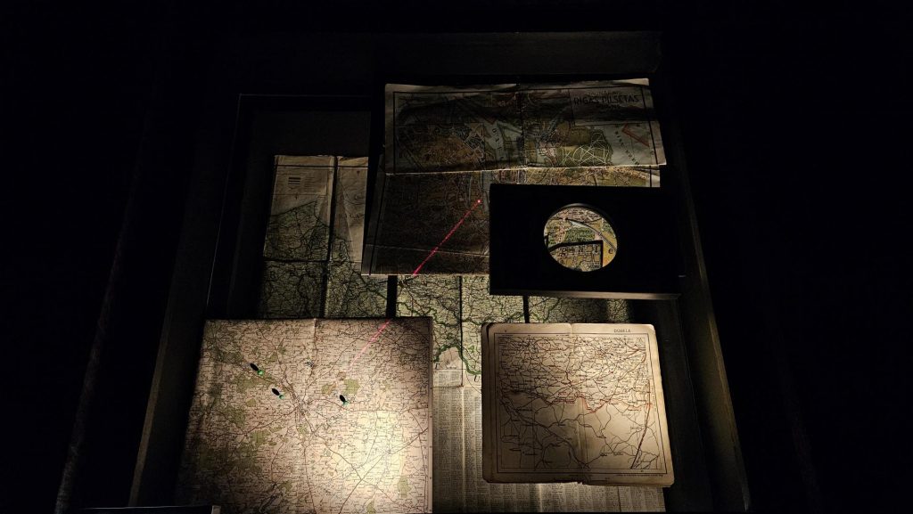 A display cabinet: a magnifying glass emphasises part of a map. Whilst a red laser joins two locations together.