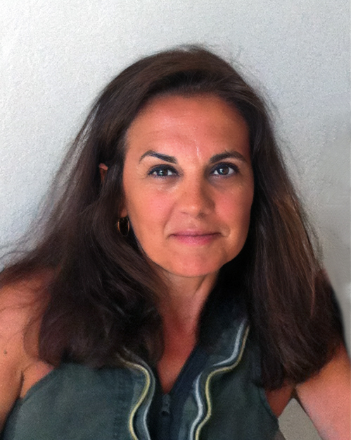 A person with long brown hair and a calm, confident expression is shown in a natural light setting against a plain background. They are dressed in a sleeveless top with subtle detailing, adding a touch of elegance. Their direct gaze and relaxed posture create a warm and approachable presence.